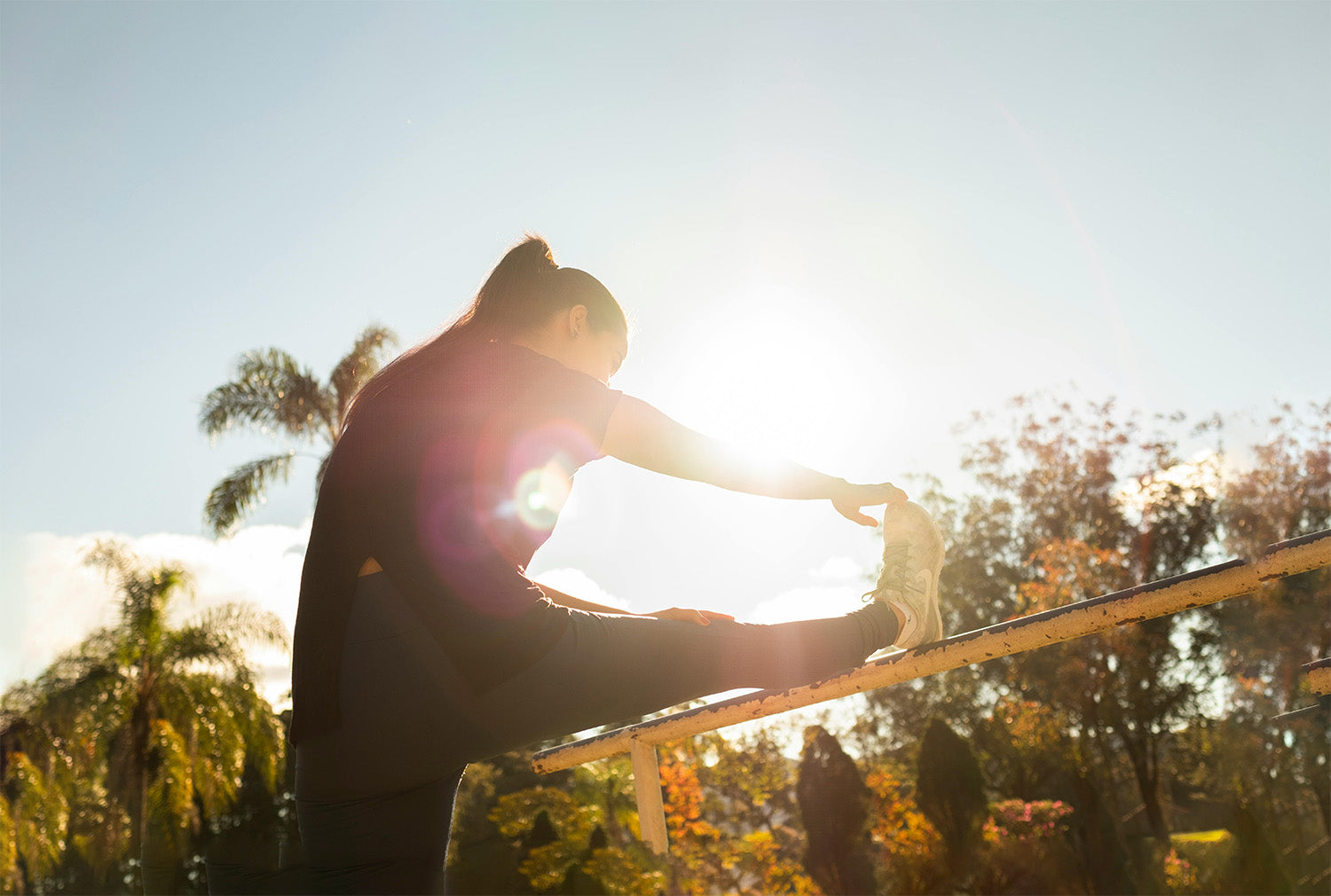 Woman stretching outdoors in sunlight with palm trees and blue sky in the background