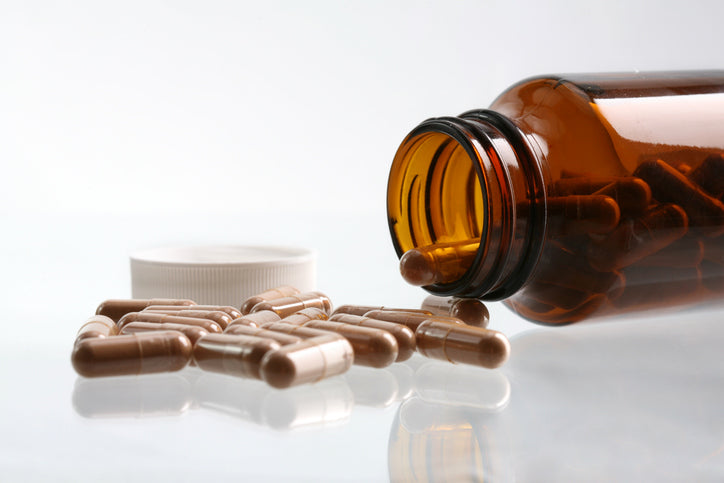 Open amber bottle with mushroom supplement capsules spilling onto a white surface, promoting natural health