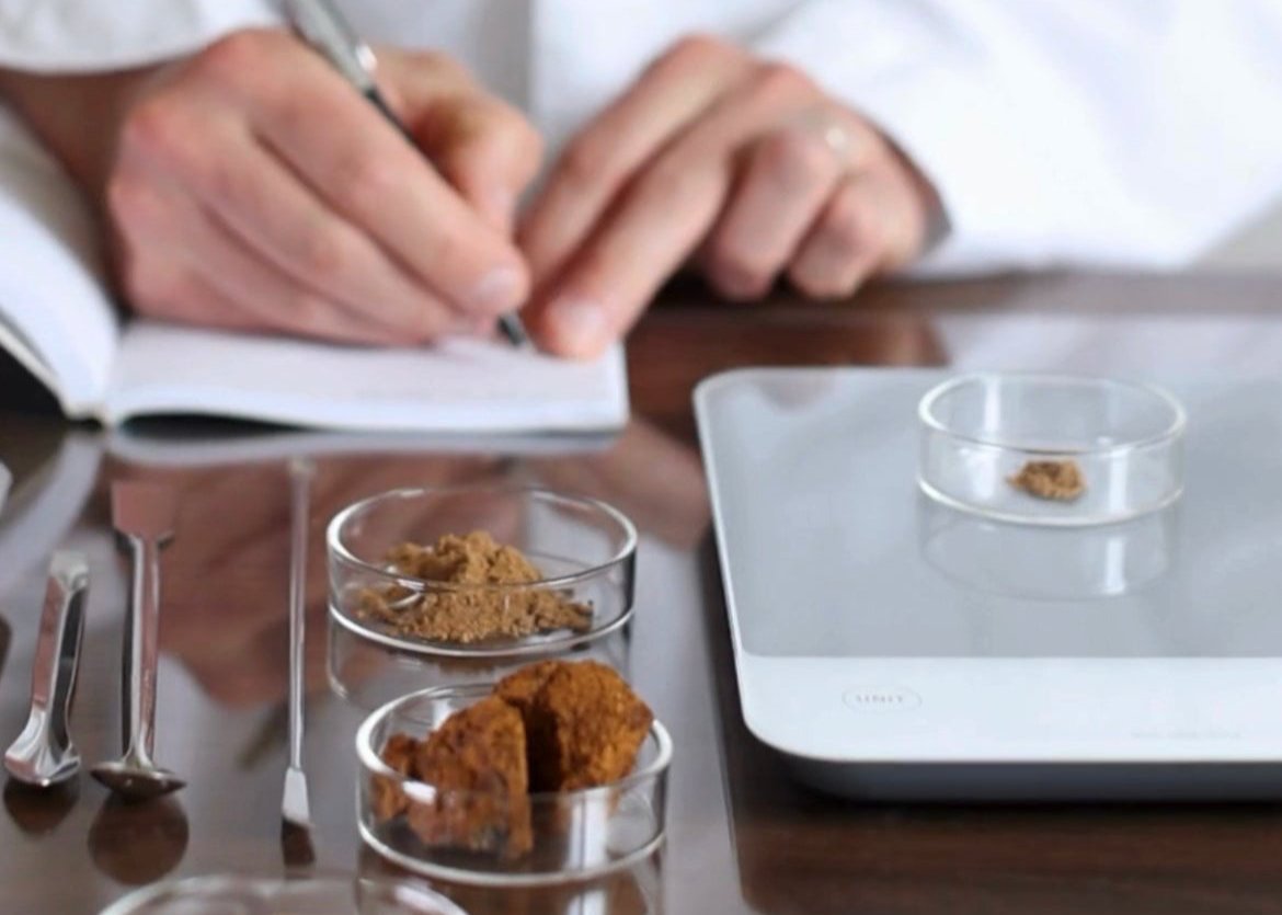 Scientist in a lab coat writing notes with mushroom extracts and powders in petri dishes on the table