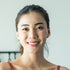 Smiling young woman Jess coach  with dark hair in a ponytail, wearing a red top, against a light background